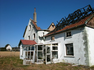 Verfallenes altes Bauernhaus mit ausgebranntem Dachstuhl vor strahlend blauem Himmel bei...