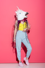 stylish woman in fashionable transparent raincoat and unicorn mask on red © LIGHTFIELD STUDIOS