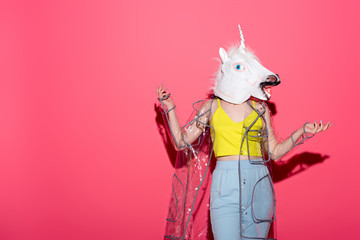 funny woman in fashionable transparent raincoat and unicorn mask on red