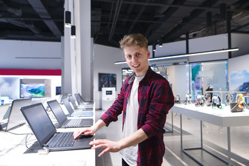 A young man buys a laptop in a technology store. Portrait of a positive young man in the...