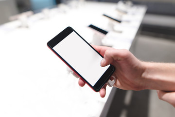 A hand with a smartphone in the mobile phone store. A white screen. A man chooses a smartphone in the store