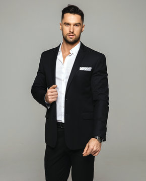 Handsome man wear black suit and white shirt posing over grey background