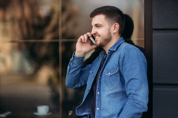 Handsome man in a denim shirt uses a phone standing on the street