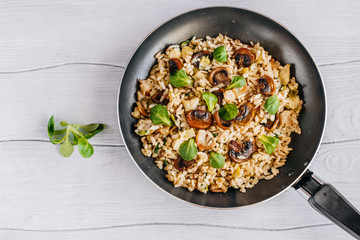 Fried rice with bacon, mushrooms and greens in a frying pan on a wooden table