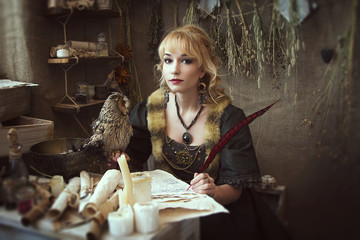 old girl in a dress at a desk with a pen in hand. On a table sits an owl with yellow eyes. Cabinet witches. Fantasy Photo