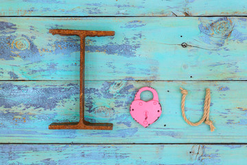 I Love You made with  iron, pink heart lock and rope hanging on antique teal blue rustic wooden background; symbolic love concept made with different texture materials