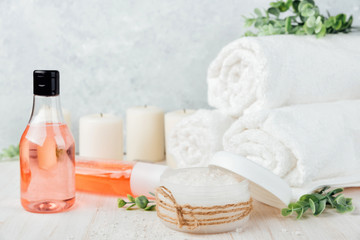 Spa composition on white wooden background. Sea salt, white rolled towels, candles, green herbs. Pink lotion and shampoo