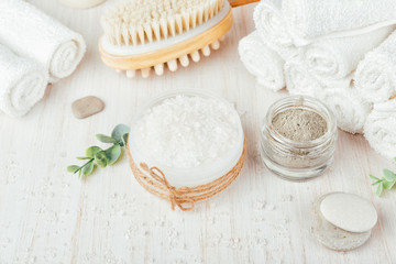 Spa composition on white wooden background. Sea salt, white rolled towels, candles, green herbs,...