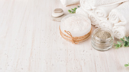Spa composition on white wooden background. Sea salt, white rolled towels, candles, green herbs, natural clay mask for face and body.