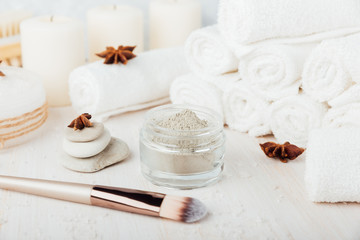 Obraz na płótnie Canvas Spa composition on white wooden background. Sea salt, white rolled towels, candles, green herbs, natural clay mask for face and body, brushes