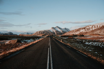 A straight road leading towards some mountains in Iceland at sunset