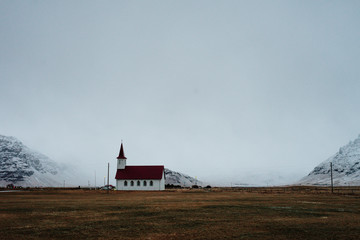 A typical Icelandic church in front of some mountains in Iceland.