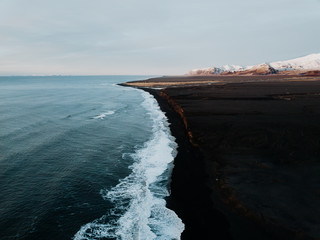 The coast of Iceland with a black sand beach and some mountains in the background, photographed...