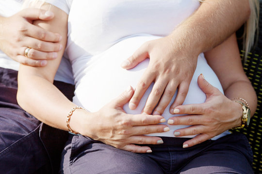 Male and female hands hold a pregnant belly