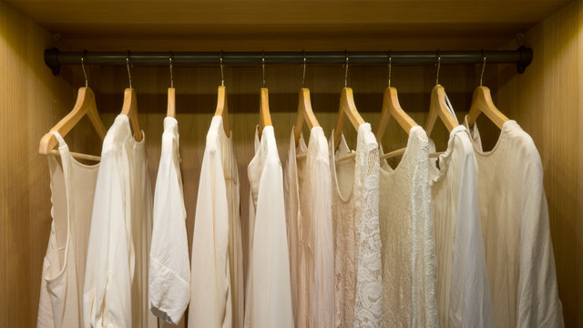 Picture taken straight into a wardrobe with lighting. White summer blouses and sweaters on hangers.