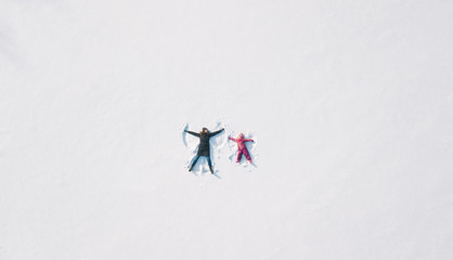Child girl and mother playing and making a snow angel in the snow. Top flat overhead view