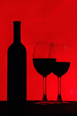 bottle of wine and glass with red wine, on red background