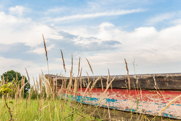 Kolorowa łódka wyciągnięta na brzeg. Kolorowy kadłub starej łodzi stojący na łące. Krajobraz z niebem. © art08
