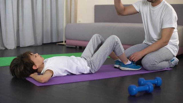 Little kid doing sit-ups and giving high five to his father, home exercising
