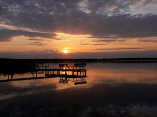 h&ouml;lzerner Steg mit Sitzb&auml;nken vor einem stimmungsvollen Sonnenuntergang am Arendsee mit dramatischen Wolken und spiegelglattem Wasser