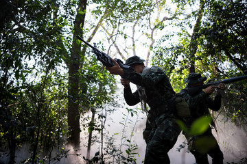 Squad of soldiers patrolling across the deep forest area and smoke background.