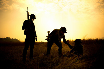 Silhouette of Military soldier holding weapons and help friend stand up.