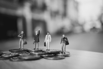 Miniature people, selective focus of business team standing on stack coins using as global business and travel concept - Black and white filter