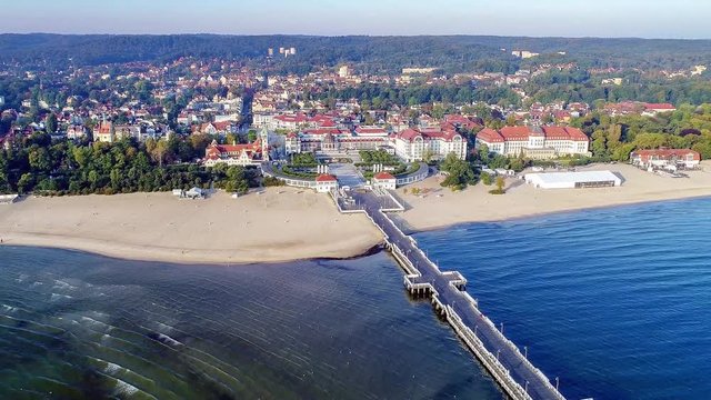 Sopot resort in Poland. Wooden pier (Molo) with promenade, marina, yachts, pirate tourist ship, beach, old lighthouse, SPA, hotels and vacation infrastructure. Aerial 4K video at sunrise