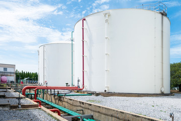Large white industrial tanks for petrochemical or oil or fuel or water in refinery or power plant or industrail plant and red fire fighting pipelines on the side of the tank on blue sky background.