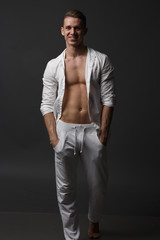 a guy with a naked torso, in white pants, and in a white shirt, stands on a gray background