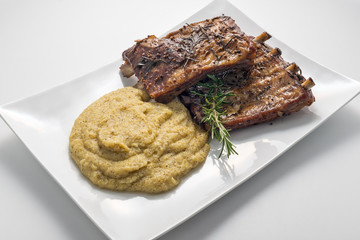 White rectangular plate with baked pork ribs and cornmeal mush