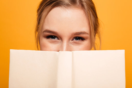 Happy young lady student covering face with book