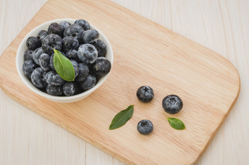 Blueberries with leaves in bowl on a wooden tray/Blueberries with leaves in bowl on a wooden tray white background. Top view