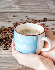 Vertical close-up photo a cup of fragrant coffee in a woman's hands against a background of coffee beans on the wood table