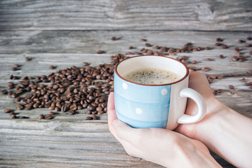 A cup of fragrant coffee in a woman's hands against a background of coffee beans and wood