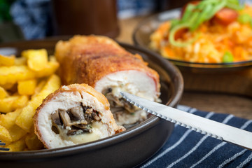 Fried chicken breast stuffed with mushrooms and cheese wrapped in ham served with fries and salad.