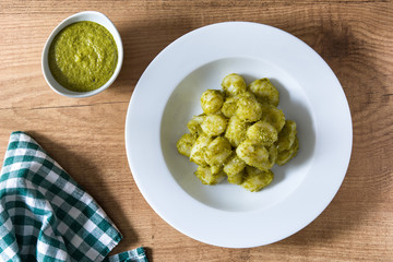Gnocchi with pesto sauce in plate on wooden table.Top view