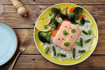 delizioso filetto di salmone cotto al vapore con verdure e riso su sfondo tavolo di cucina rustico