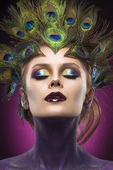 Beautiful big breast girl wearing peacock feathers in her hair and artistic violet shiny body art on her neck, vanguard makeup