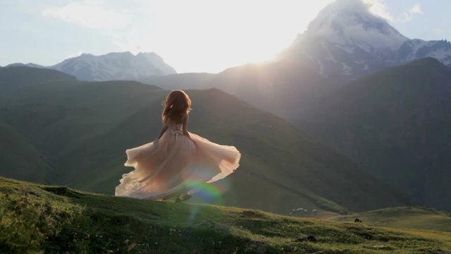 beautiful girl in a chic dress dances in the evening against the backdrop of the mountains and the setting sun