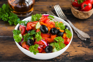 Healthy vegetarian salad with fresh vegetables in a white bowl on the wooden table.