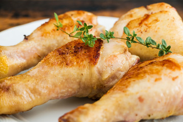 Roasted chicken drumsticks and fresh thyme on a white plate.