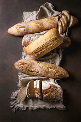 Variety of loafs fresh baked artisan rye, white and whole grain bread on linen cloth over dark...