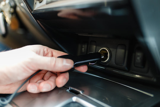 A man connects the device to the cigarette lighter of the car. The man's hand is plugging the car camera or phone adapter into the cigarette lighter into the car.