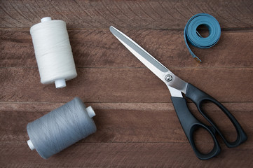 Sewing thread scissors and tailor meter on rustic background