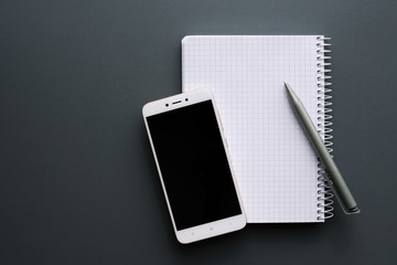 blank white notebook with smartphone and pen over gray desk