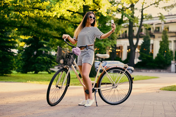 Naklejka premium An attractive brunette female with a bicycle in the city park.