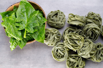 Fresh spinach with green pasta on a gray background.