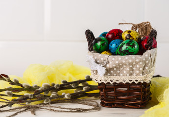 colored quail eggs for Easter in a wicker box with willow branches