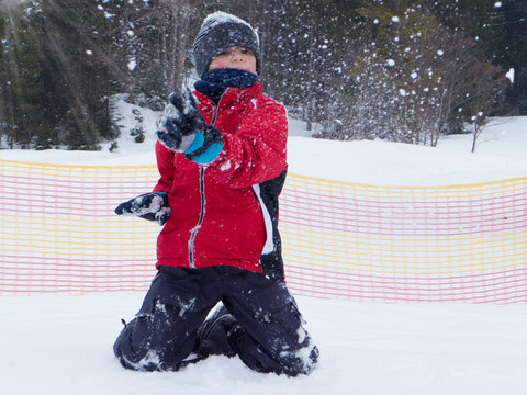 Im Schnee kniender Junge wirft mit Schnee